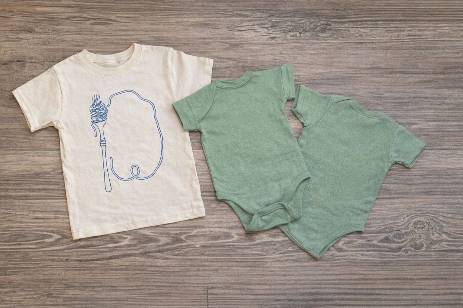 Kremowy t-shirt z nadrukiem widelca i dwa zielone body dziecięce.